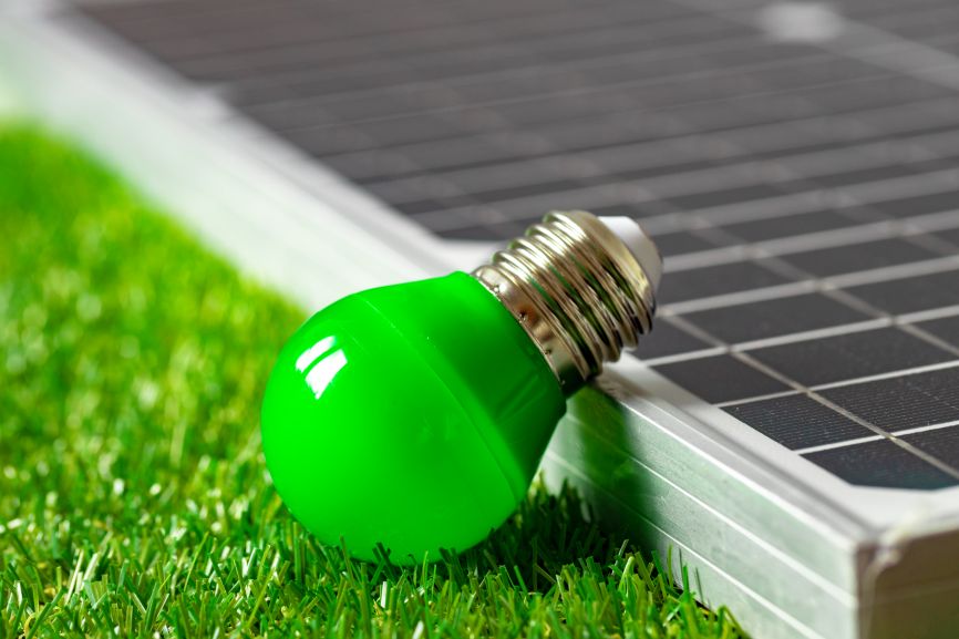 Green light bulb beside an EcoSunWorks solar panel representing solar panels and power outage solution